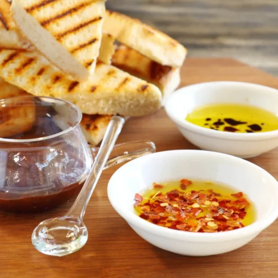 Two bread oils in bowls on a serving platter next to pieces of grilled bread.